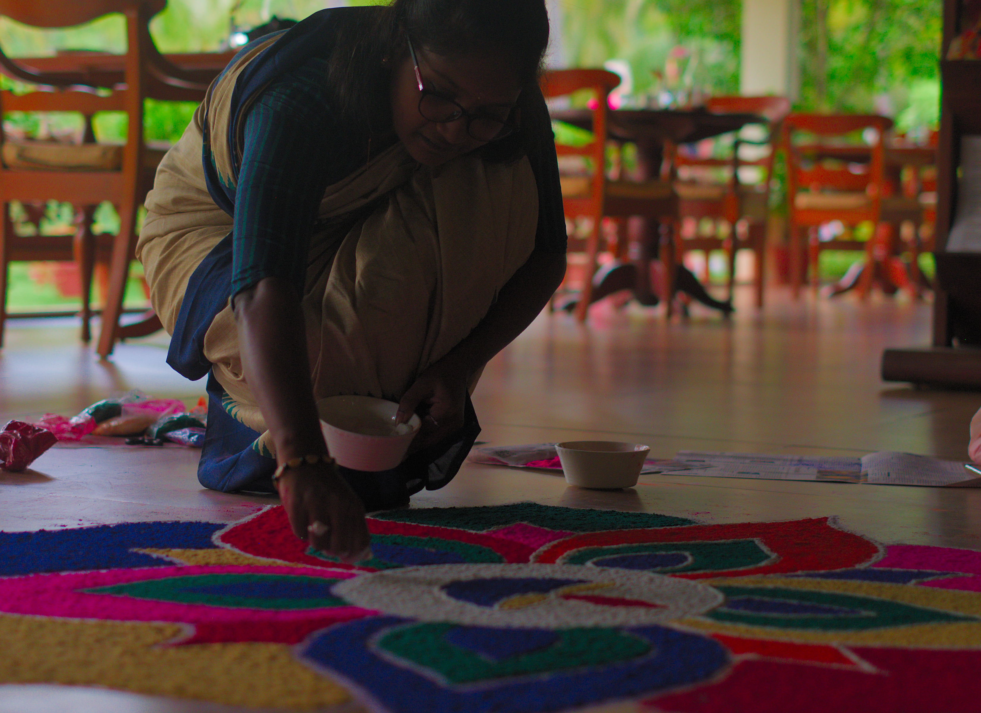 Eine Frau gestaltet zum Onam-Fest ein farbenfrohes Pookalam aus Blüten im The Nattika Beach Ayurveda Resort