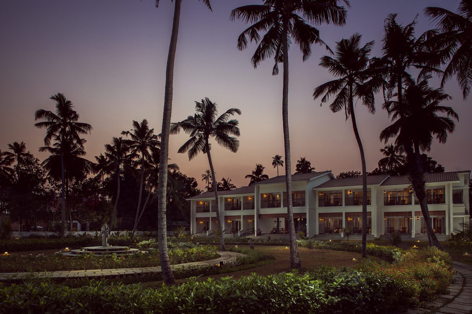 Das Amal Tamara Ayurveda Resort zeigt sich im Abendlicht mit tropischem Garten und elegantem Hauptgebäude.